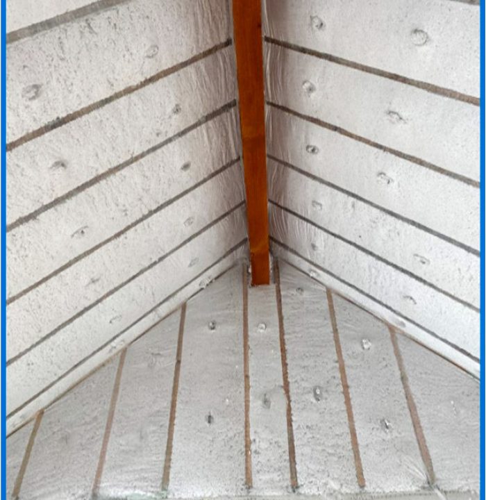 A detailed shot looking down into the corner of a room where the walls and floor meet. The surfaces are covered with insulation panels that have been sprayed with foam, showing how every angle and joint is meticulously sealed for maximum performance.