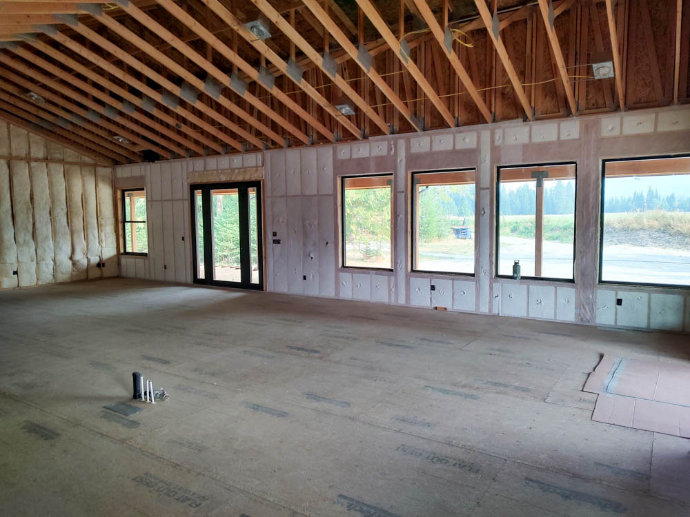 Looking directly up at the peak of a complex wooden roof structure. Spray foam insulation has been applied to the sheathing between the numerous intersecting rafters, showcasing the precision needed for such detailed framing.