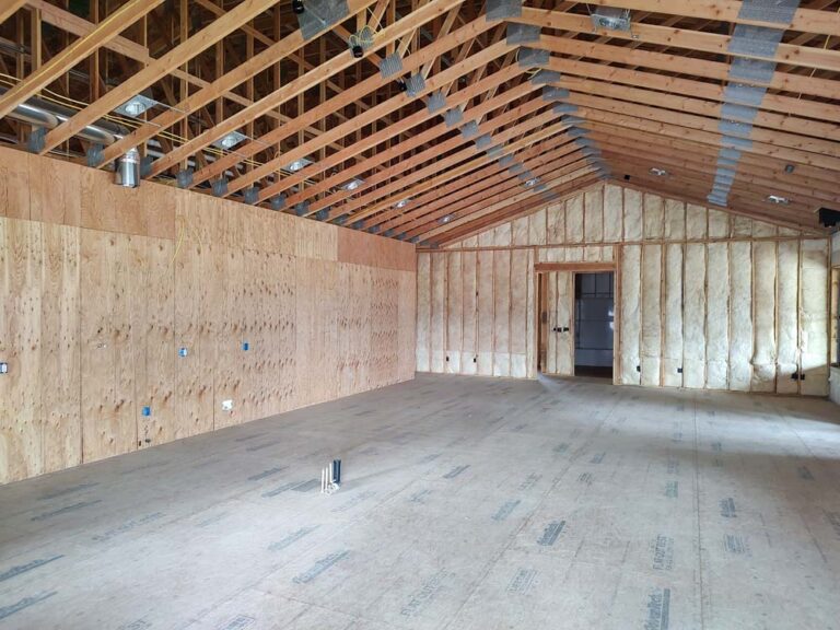 A close-up view of a finished interior wall in a steel-framed building. The cavities between the metal studs are completely filled with thick, textured spray foam insulation, creating a continuous thermal barrier.